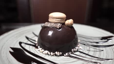 gourmet dessert on a black plate spins. little macaroon with a piece of chocolate. rotating food. presentation of the dish