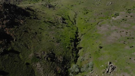 Aerial-revealing-shot-of-old-eroded-mountain-range-over-a-winding-road-on-a-sunny-clear-day