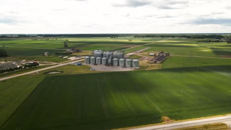 aerial view of agro silos tower of storage of agricultural products and grain elevators in the middle of a green cultivated field, sliding shot