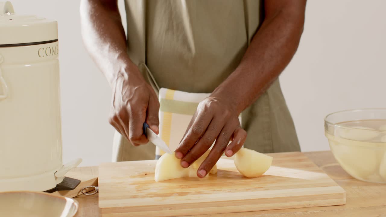 Man in olive apron placing peeled onion, slicing with knife on cutting board for cooking