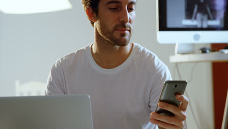 fotógrafo masculino usando un teléfono móvil mientras trabaja en una computadora portátil 4k