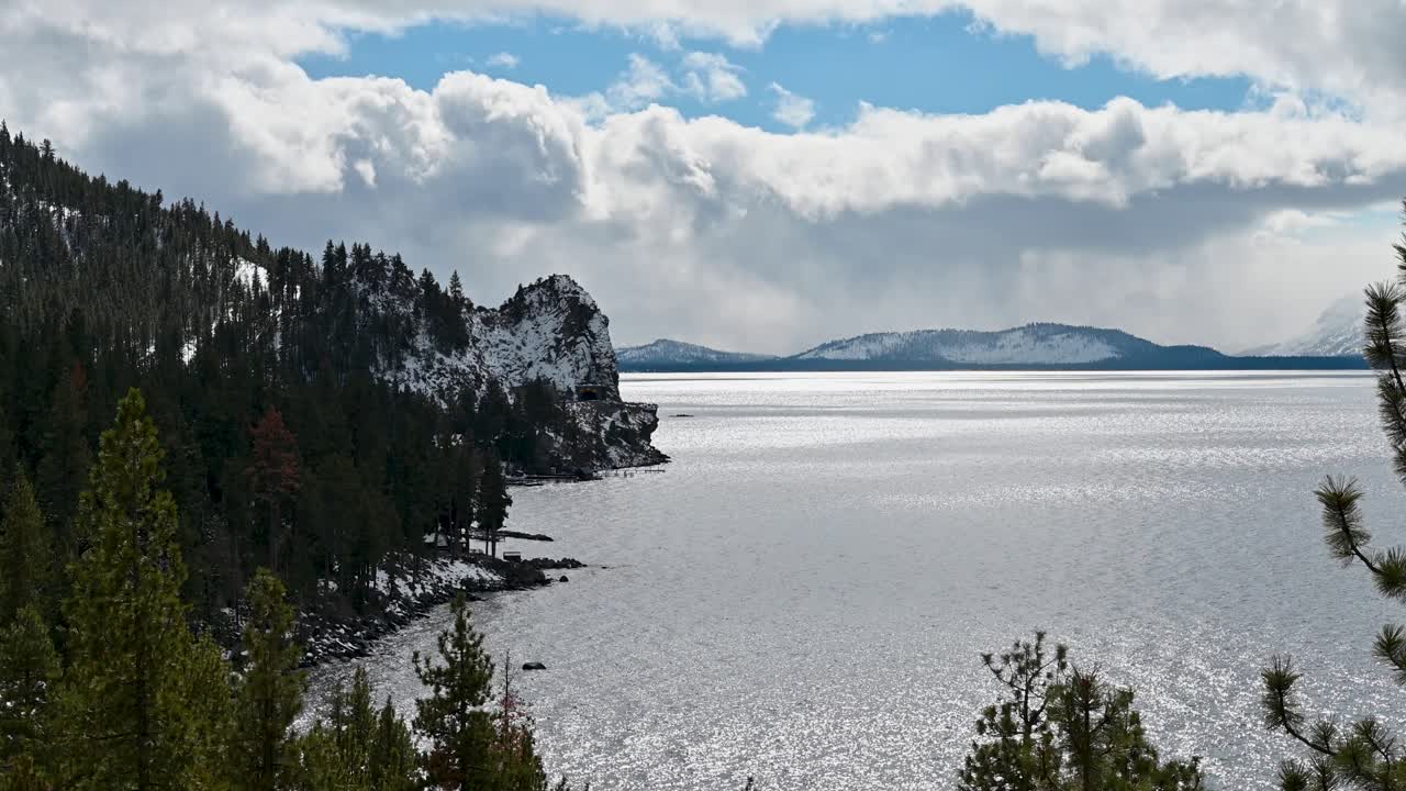 Rugged forested cliffs descend into a vast mountain lake with dramatic cloud formations above