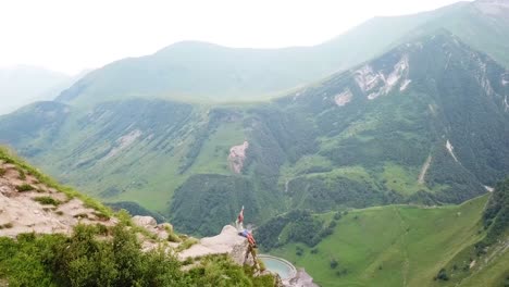 aerial as a man sits on a cliff overlooking a gorge and countryside of the republic of georgia