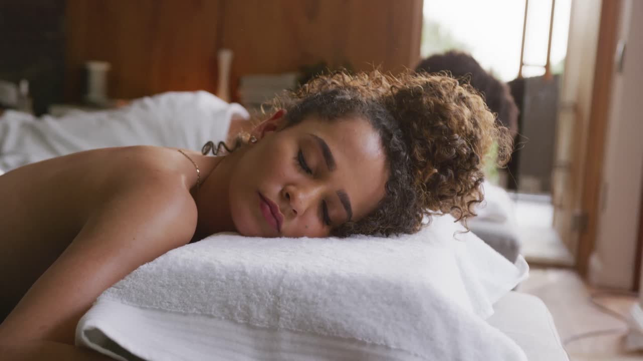 Video af et afslappet mangfoldigt par, der ligger med lukkede øjne på massagebrikse på et wellnesscenter.