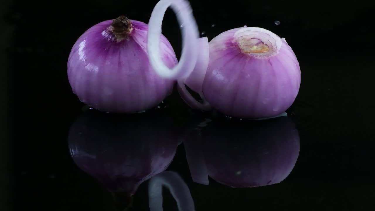 Two peeled red onions with an onion ring on a wet surface