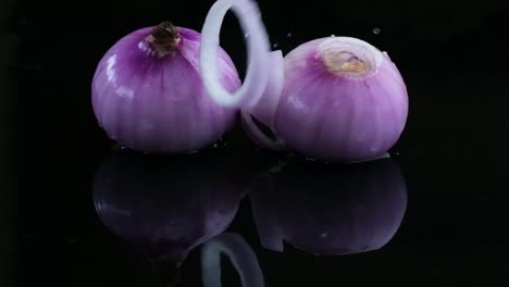 two peeled red onions with an onion ring on a wet surface