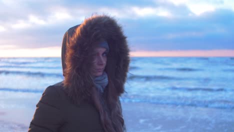 Young-woman-in-winter-clothes-walks-along-the-sandy-shore-of-the-Baltic-sea-beach-at-romantic-sunset,-medium-jib-shot-up