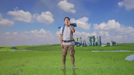 full body of asian male hiker with mountaineering backpack screaming holding hands near his mouth while traveling in stonehenge