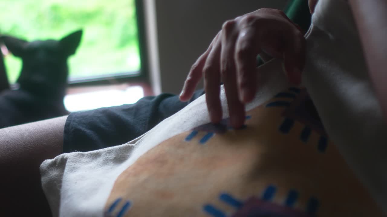 Woman's hand resting on a patterned fashion bag, showcasing a trendy lifestyle accessory inside a home with natural daytime light entering through the window