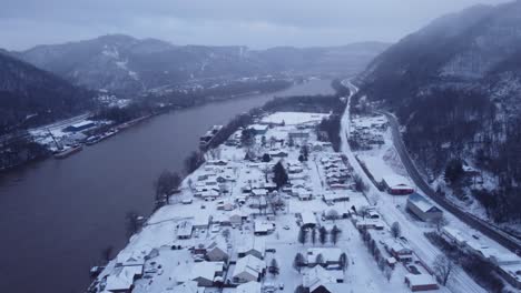 dron volando sobre una ciudad montañosa al lado de un río con nieve por todas partes