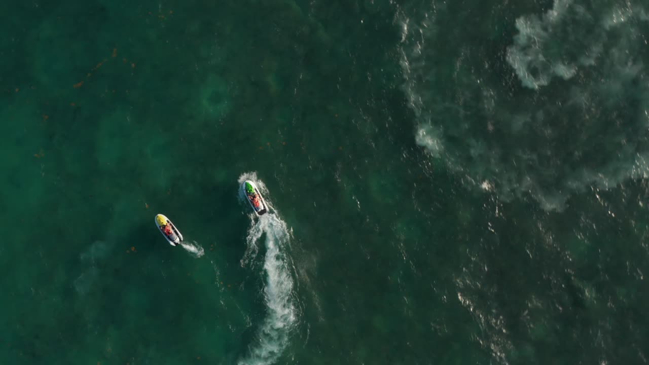 제트 스키가 다른 물놀이기를 둘러싸고 돌아다니고 있다. 공중  ⁇ 에서 내려다보는 모습. 카리브 해 위를 회전하는 드론