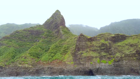 4K-Hawaii-Kauai-Boating-on-ocean-floating-left-to-right-past-peak-and-cave-with-mountain-in-cloudy-distance