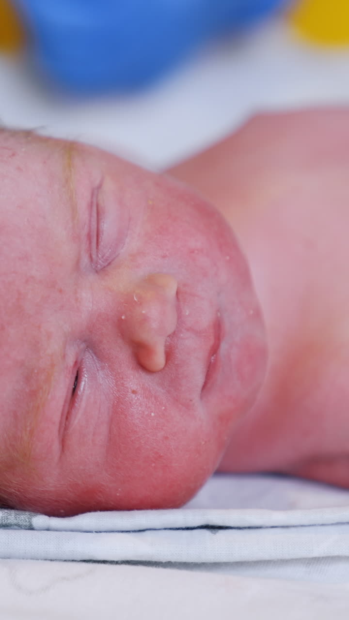 Tiny cute Caucasian newborn with red hair. Just born baby slightly opening its eyes. Close up. Vertical video