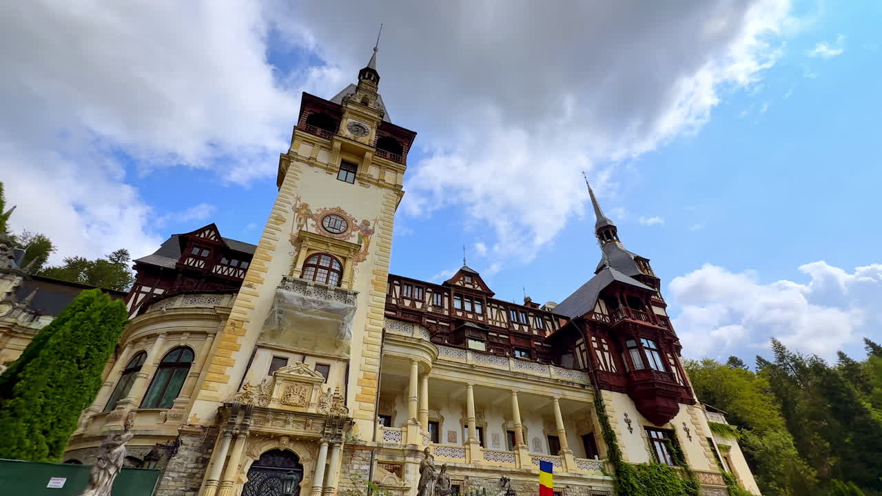 Sinaia, Romania, 17 July 2025: Gorgeous façade of the Peles Castle in Sinaia, Romania from low angle view. Fluffy clouds at backdrop
