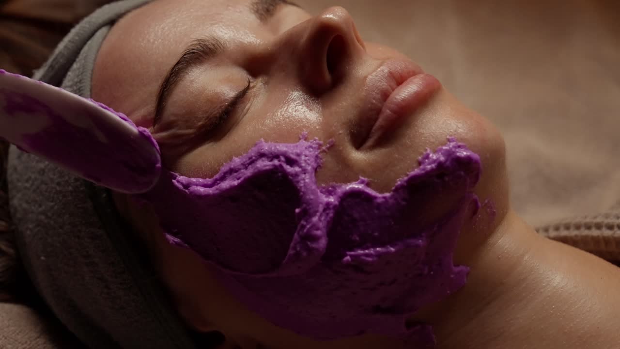 Gros plan d'une femme recevant un traitement de masque facial violet dans un spa