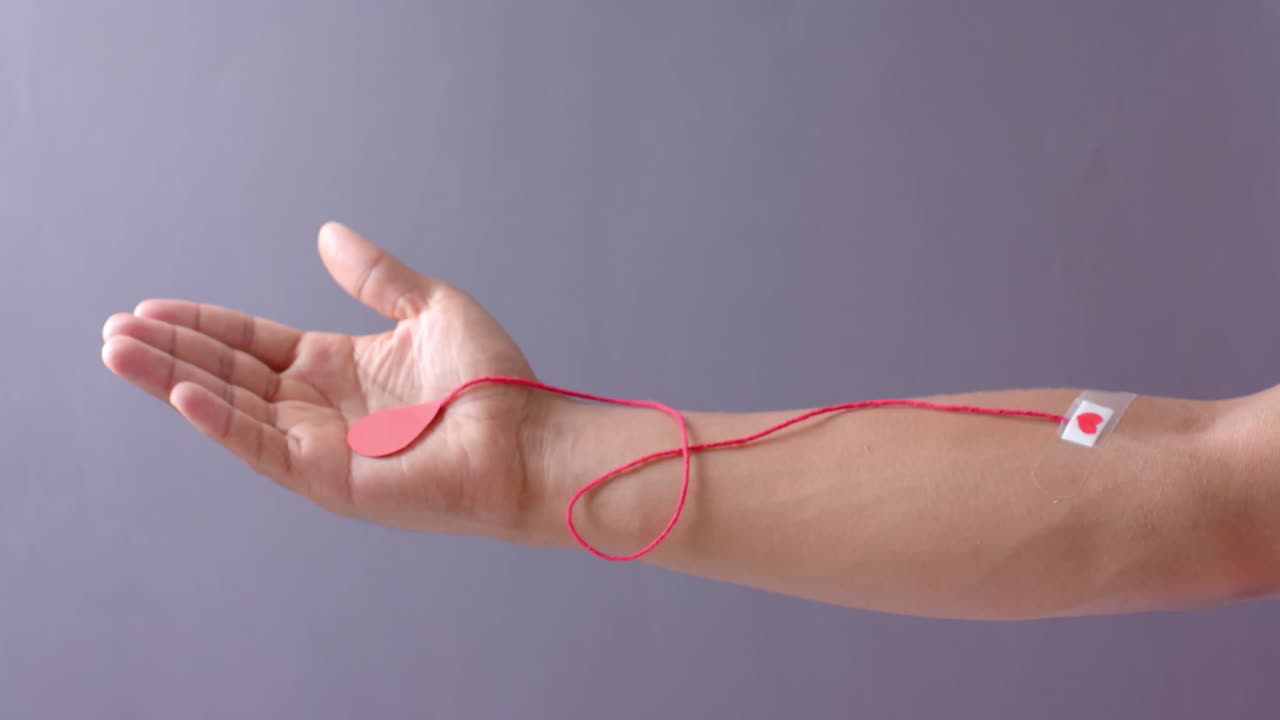 Hand of biracial man with blood drop, red string and heart sticking plaster on grey, slow motion