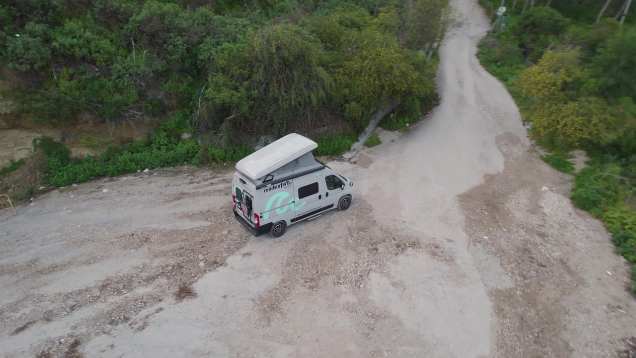 Aerial point of interest shot of a van in a dirtroad in the middle of a grass field in Lisbon.