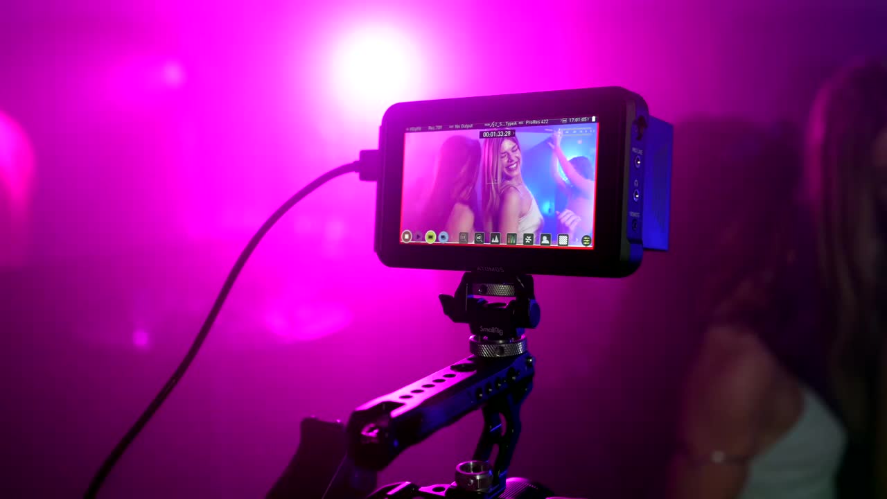 Camera monitor displaying video of women dancing with purple lighting