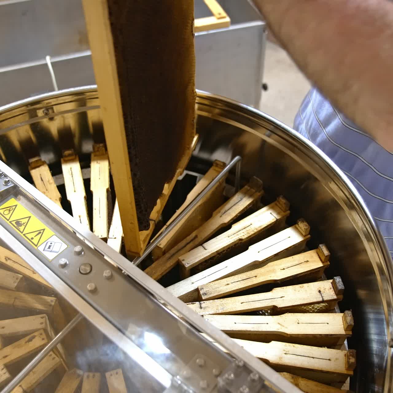 Mani maschili scaricano telai da miele in un apparecchio per l'estrazione del miele. Raccolta del miele in un allevamento di api. Primo piano