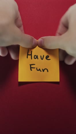 hands posting have fun sticky note on red wall, highlighting enjoyment