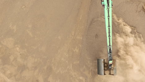 top-down aerial view of a mechanical arm creating a cloud of sand dust as it excavates the sandy terrain