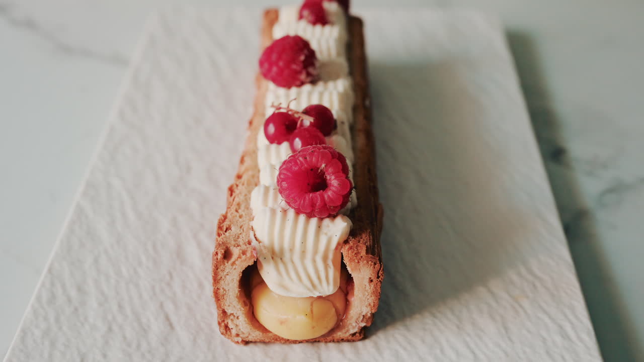 Close up of a gourmet pastry topped with cream, raspberries, and red currants