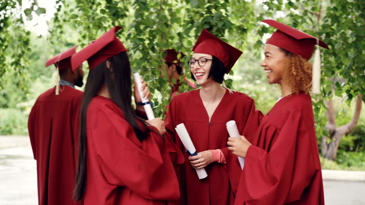 Compagni di studi parlano e ridono dopo la cerimonia di laurea, tenendo in mano i diplomi e indossando toche e tocco; le ragazze condividono ricordi ed esprimono speranze