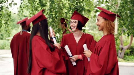 fellow students are talking and laughing after graduation ceremony holding diplomae and wearing gowns and mortarboards, girls are sharing memories and expressing hopes.