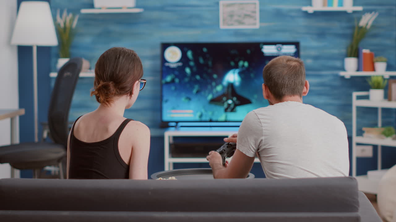 Girlfriend eating popcorn and supporting boyfriend gamer playing console video game first person shooter on tv