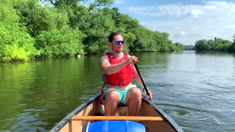 Athletic-man-in-red-buoyancy-vest-paddles-canoe-on-river-wye-in-sun