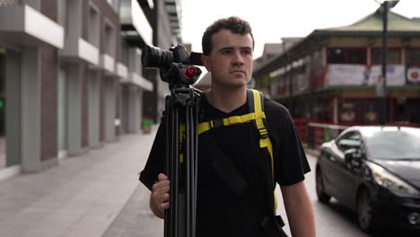 Young-man-is-walking-the-streets-of-London-with-his-camera-and-tripod,-looking-for-a-good-shot
