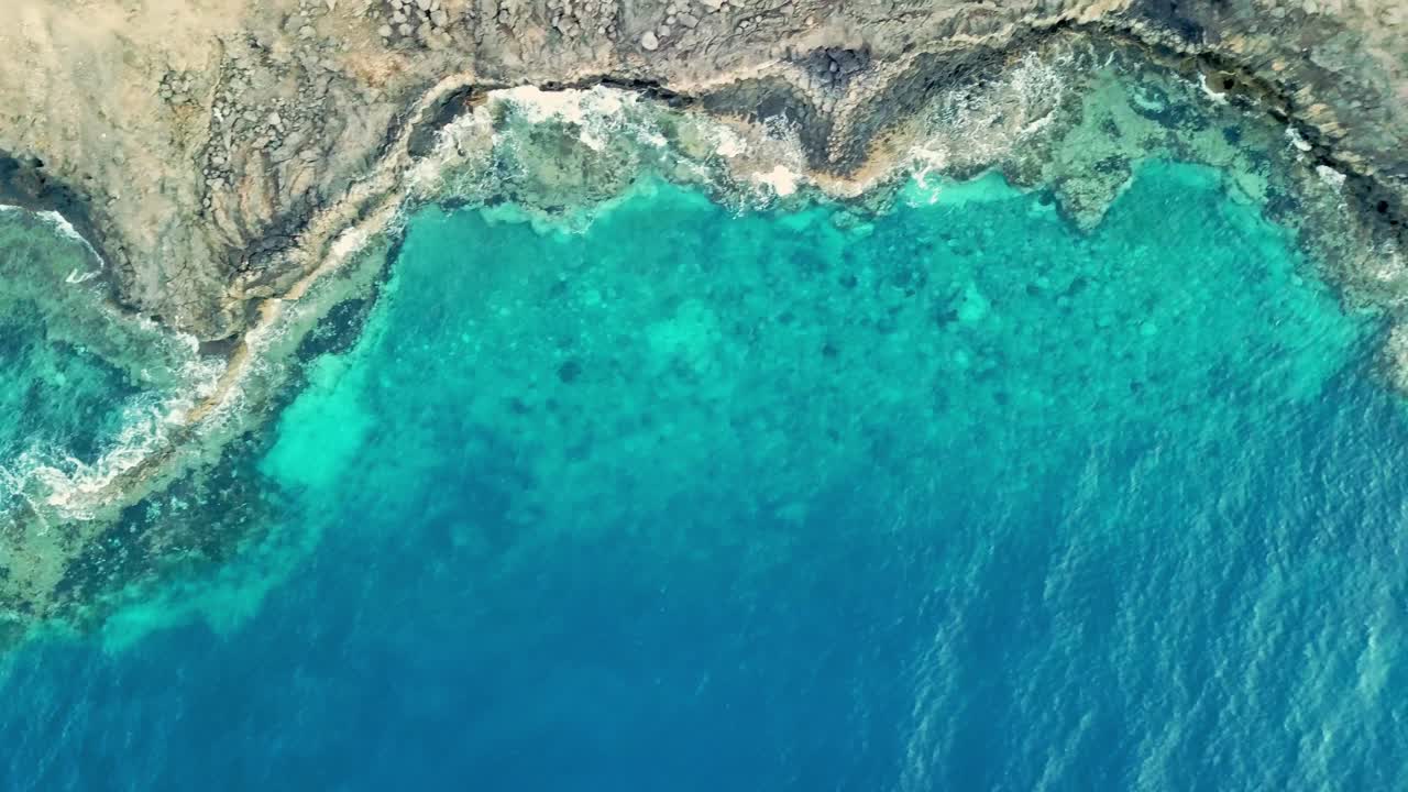 Drone shot over Lanzarote cliff egde with ocean sea waves breaking against rocks in Puerto Del Carmen - crystal clear blue water - left to right