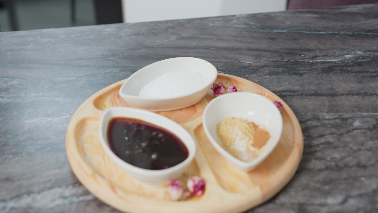 세련된 드레스를 입은 여성이 검은색 끔한 테이블에 점심 식탁을 세우고, 소스, 향신료, 소금이 들어있는 세라 그과 함께 나무 트레이, 건조한 꽃으로 장식되어 있습니다.