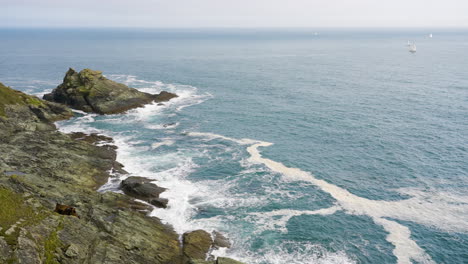 rocky coastline with waves and sailboat