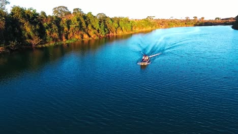 a small fishing boat travels down a deep blue river in the evening sun, slow motion aerial drone shot