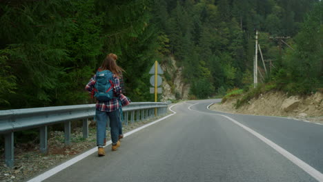 couple hitchhikers walk mountains. two travelers trekking on roadside highway.