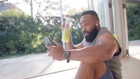 happy african american man resting making video call using smartphone at sunny home, slow motion