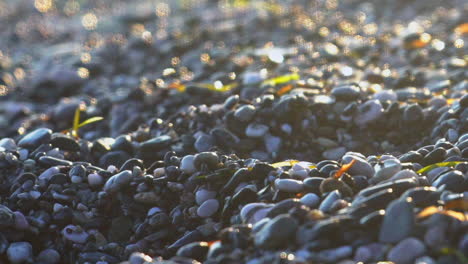 Nahaufnahme-Von-Glänzenden-Kieselsteinen-Am-Strand-Von-Kalamata,-Neigung-Zeigt-Verschwommene-Wellen-In-Zeitlupe-Mit-120-Bildern-Pro-Sekunde