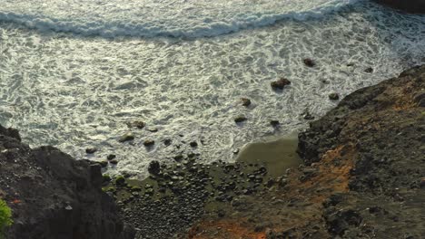 las olas ruedan en una playa rocosa aislada con acantilados de la bahía en la luz del sol de la tarde