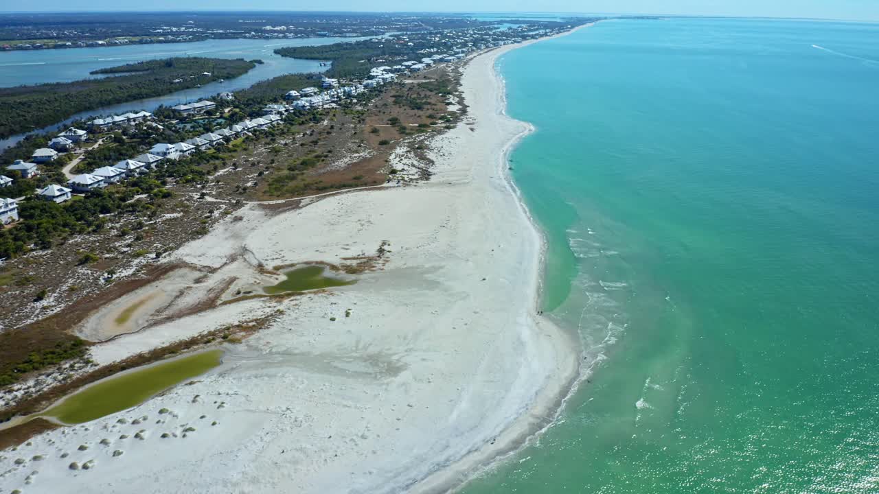 White sandy beach stretches along the coast beside a residential area with greenery and small water inlets under a partly cloudy sky, Florida