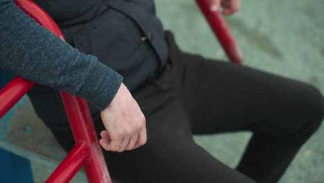 close-up of a person sitting on workout equipment, hands resting on the red bars while he shake his leg