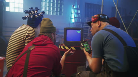 group of men watching an old monitor and smartphone in a warehouse