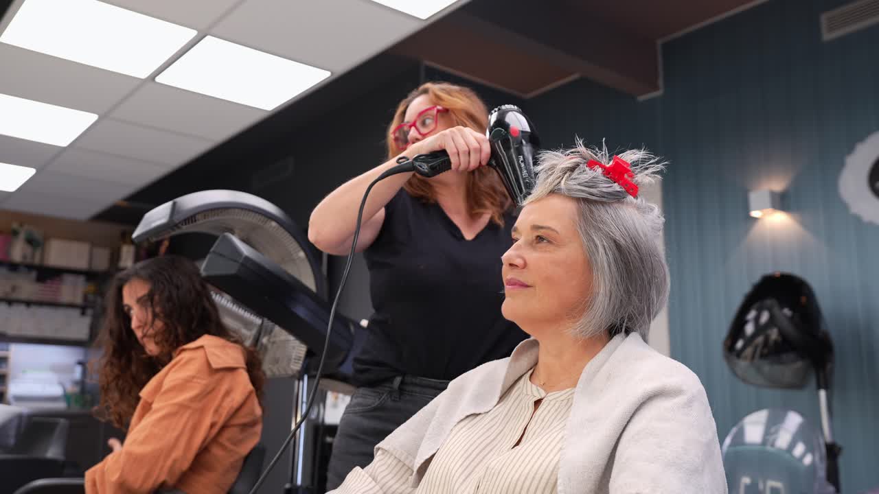 Professional Hairdresser Blow Drying a Mature Woman's Hair in Salon
