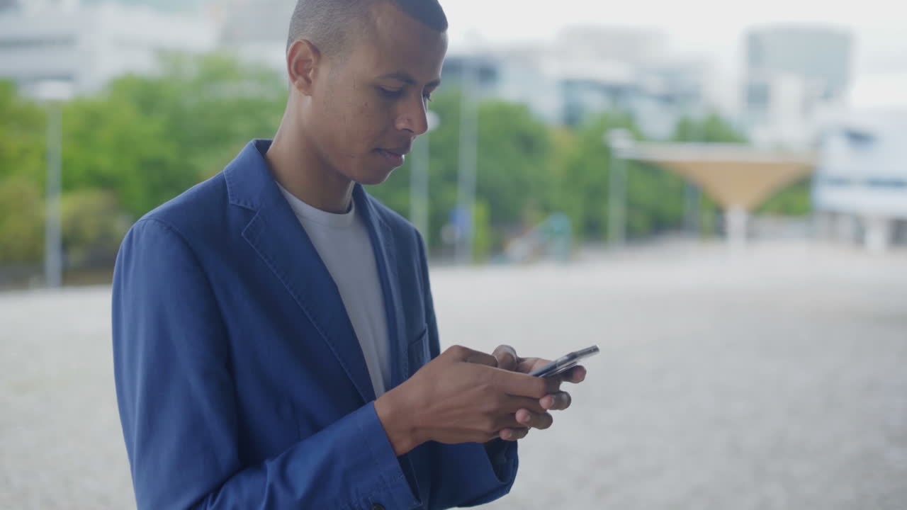 Smilende afroamerikansk mand taster besked på smartphone