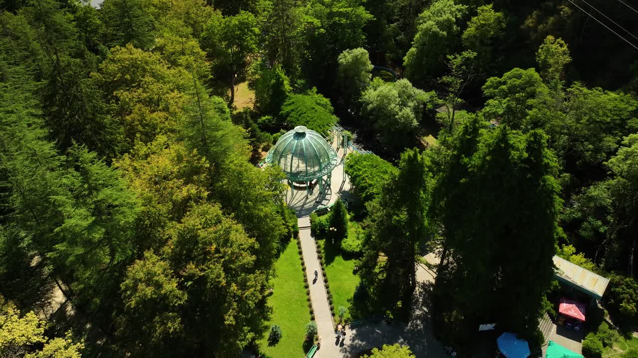 A direct aerial view of a circular glass pavilion surrounded by dense green forest, pathways, and well-organized garden landscaping