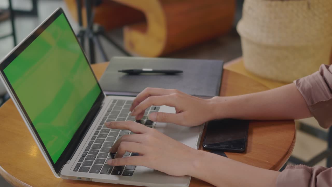 mujer de negocios sentada sola trabajando escribiendo en el teclado de una computadora portátil pantalla verde en una cafetería