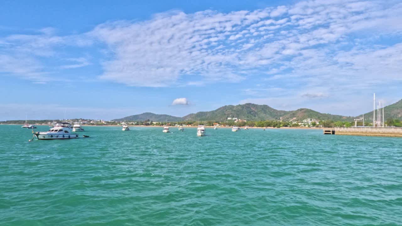 푸켓의 라와이 해변에서 밝은 하늘 아래 푸르키즈색 물을 가로질러 움직이는 배의 조용한 풍경