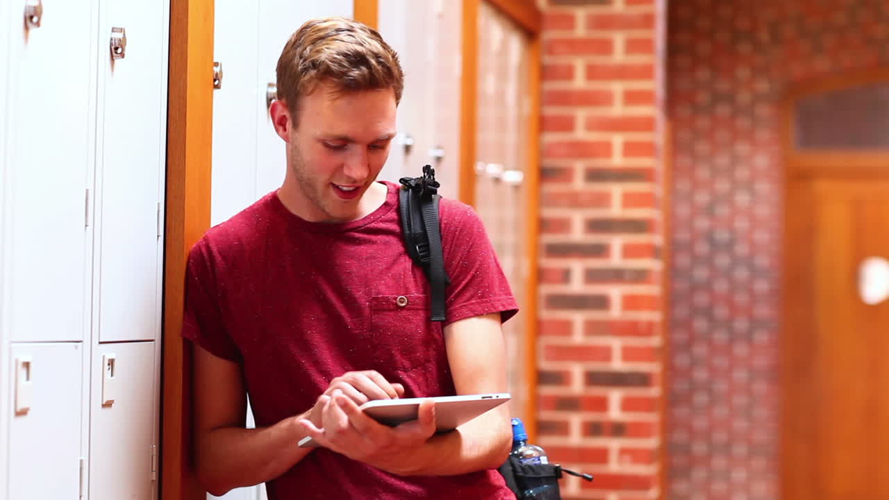 Estudante feliz usando tablet encostado em um armário