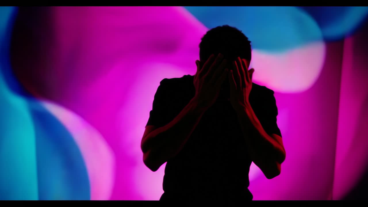 Silhouette di una persona con le mani davanti al viso su uno sfondo astratto colorato