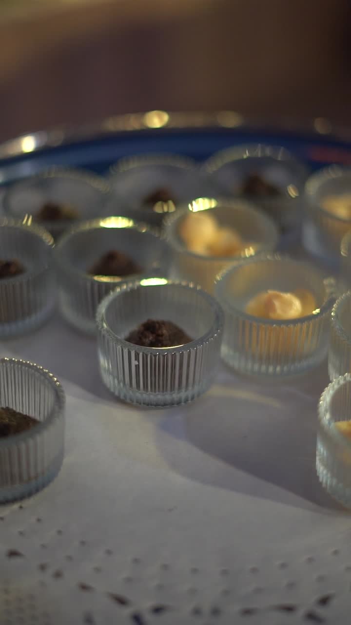 Små glaskopper fyldt med forskellige fløde- og chokoladeblandinger arrangeret på en bakke, nærbillede.